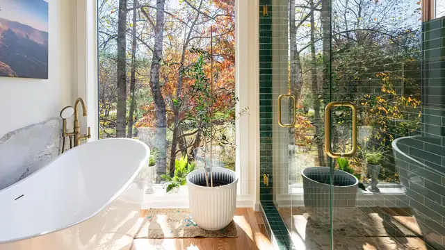 Primary bathroom remodel with freestanding soaking tub, brass faucet, green tile shower and a floor-to-ceiling window onto fall woods