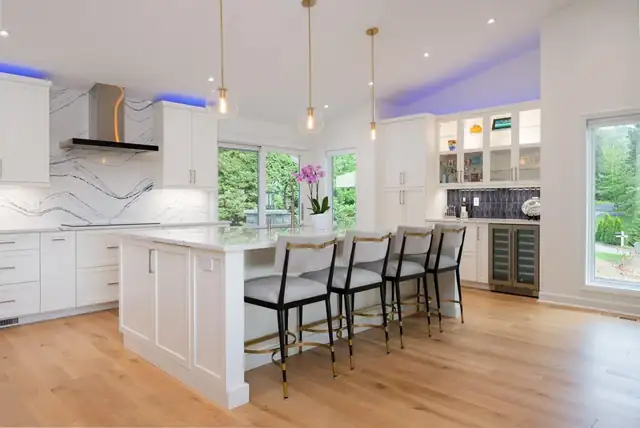 Remodeled kitchen with white shaker cabinets, marble-look slab backsplash, long island with black stools and oak floors