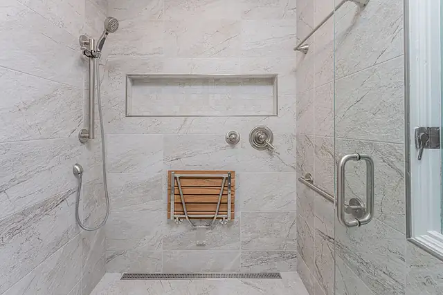 Curbless shower with fold-down teak seat, grab bar, handheld shower and linear drain in marble-look porcelain tile
