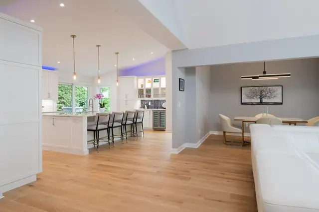 Open kitchen and dining room with a long white island, pendant lights, wine fridge and wide-plank oak floors
