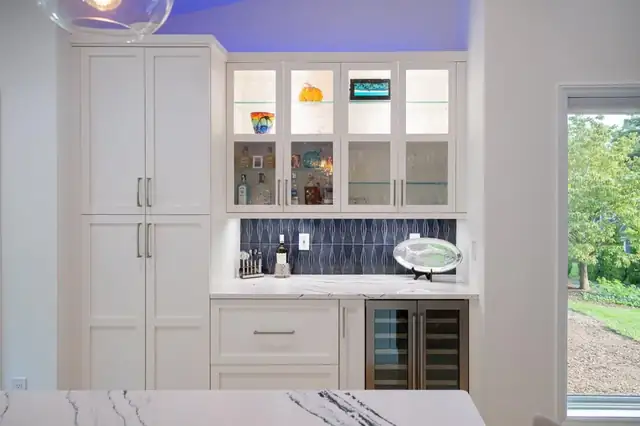 Built-in bar with white cabinets, glass-front uppers, a navy tile backsplash and a wine fridge