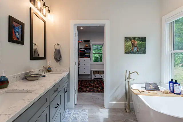 Primary bathroom with slate blue vanity, quartz top, freestanding tub and a doorway into the walk-in closet